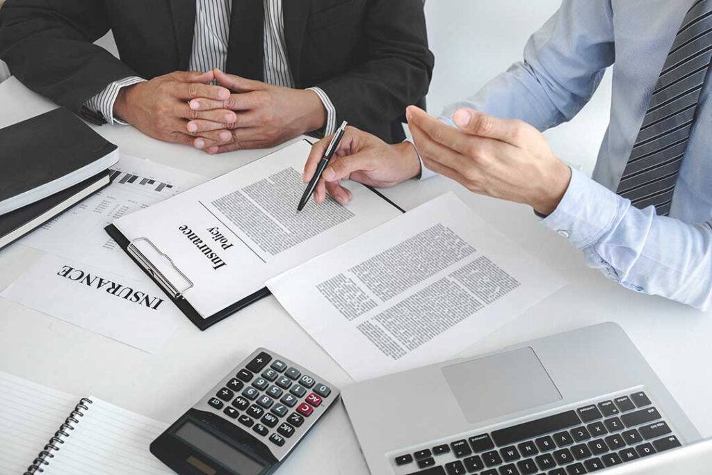 A person completing a life insurance application with medical documents and a pen at a kitchen table.