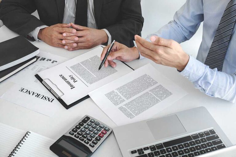 A person completing a life insurance application with medical documents and a pen at a kitchen table.